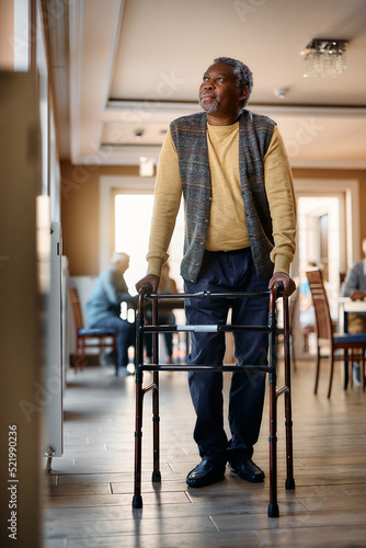 Senior black man using walker while standing by window at nursing home. photo