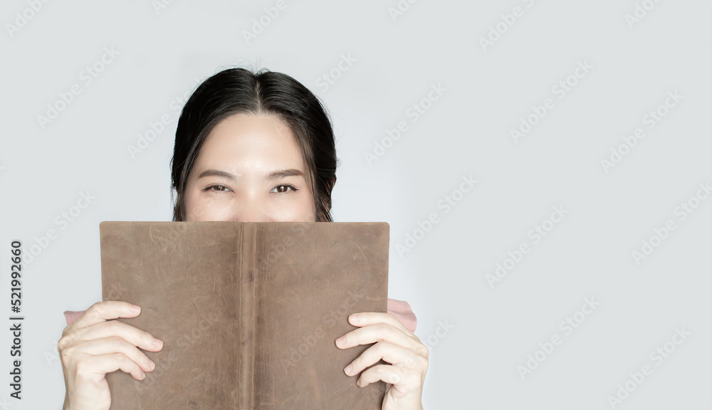 Asian beautiful woman is holding the book covering face express her happiness during reading a journal or literature.