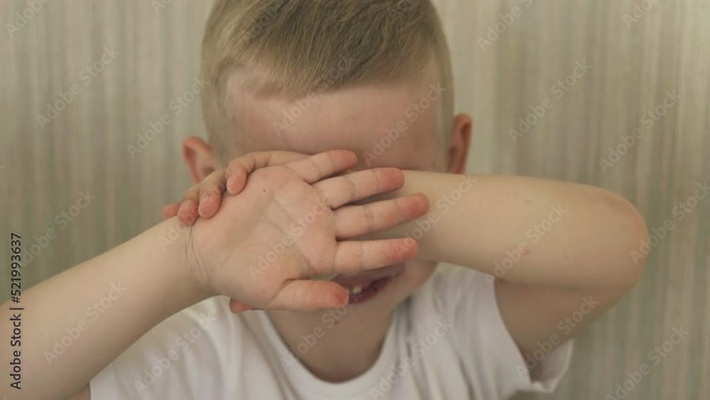 The boy covers his face with his hands, smiles, closes his eyes. Close-up. The boy covers his face with his hands, smiles, closes his eyes. Close-up.