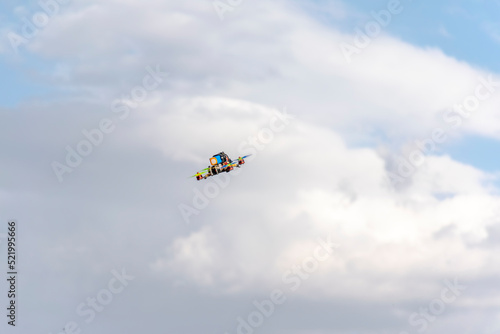 Flying quadcopter drone with blue cloudy sky in background. Low angle view of the multi-colored unmaned vehicle in the air.