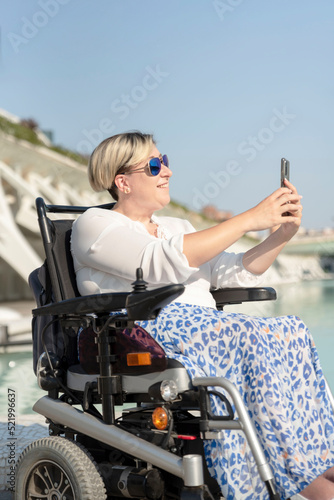vertical portrait of a smiling woman with disability in a wheelchair with sunglasses taking a selfie photo