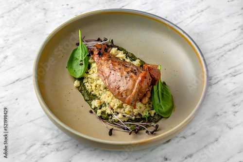 Fillet of rabbit or duck with couscous or bulgur with spinach sauce in a  plate on a marble background. Restaurant banquet menu.