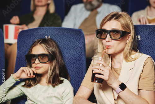 Mature Caucasian woman and her preteen daughter wearing polarized 3D eyeglasses watching film at cinema photo