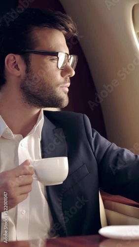vertical video of businessman holding coffee and looking at illuminator while traveling by plane
