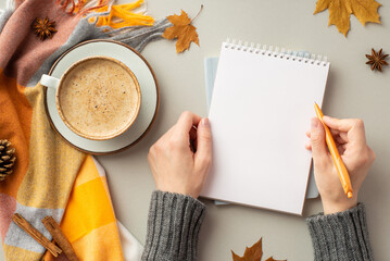 First person top view photo of girl's hands in sweater writing in reminder cup of coffee saucer plaid yellow maple leaves pine cone anise cinnamon sticks on isolated grey background with empty space