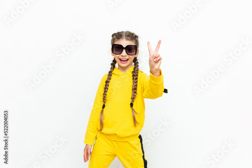 A beautiful little girl in a yellow tracksuit, with pigtails on her head and sunglasses on a white isolated background. © Юлия Дьякова