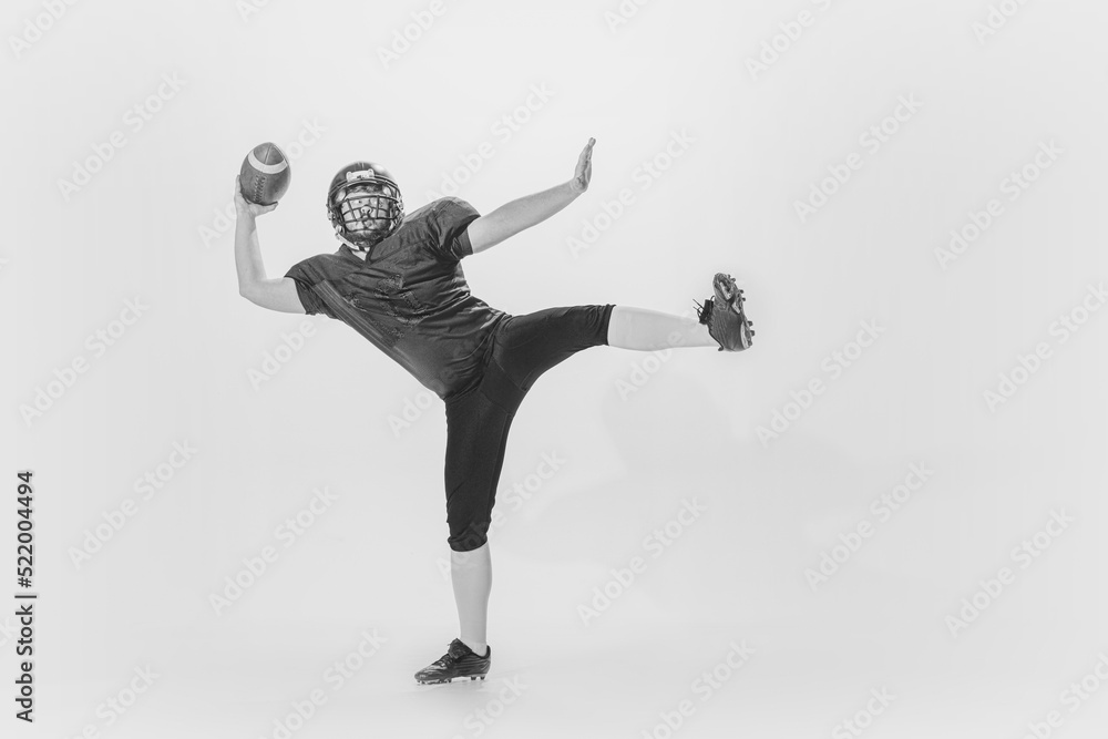 Studio shot of american football player training with ball isolated on white background. Concept of sport, achievements, retro style. Monochrome