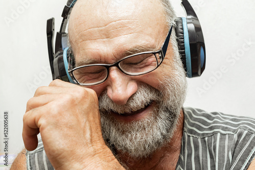 Photo of an impressed pensioner with a sincere laugh, listening to music in headphones on a white background, close-up