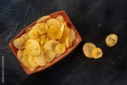 Potato chips or crisps, a salty snack, shot from the top on a black slate table