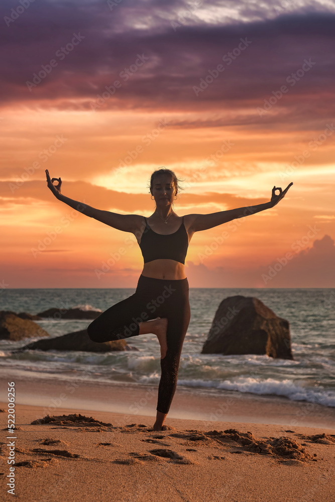 Woman yoga position arms raised on tropical sea coast or ocean beach outdoors at sunset
