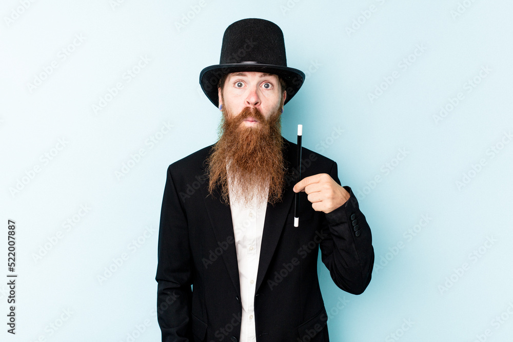 Fototapeta premium Young magician man isolated on blue background shrugs shoulders and open eyes confused.
