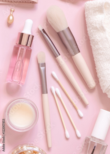 Skin care products and make up brushes on light pink, top view