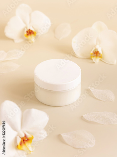 Cream jar with a blank white lid near orchid flowers on light yellow close up. Cosmetic Mockup