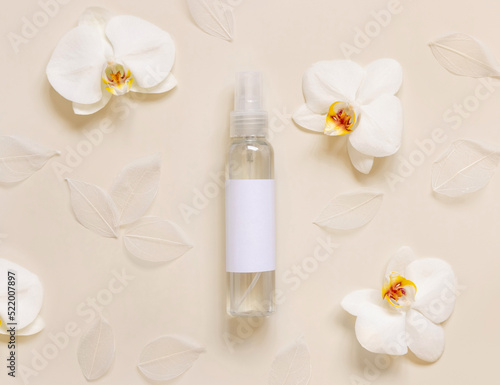 One pump dispenser bottle near white orchid flowers on light yellow top view. Mockup