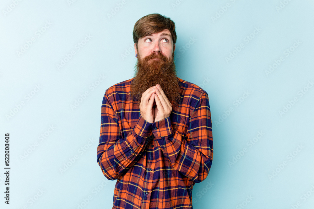 Young caucasian red-haired man isolated on blue background holding hands in pray near mouth, feels confident. Young caucasian red-haired man isolated on blue background holding hands in pray near mouth, feels confident.