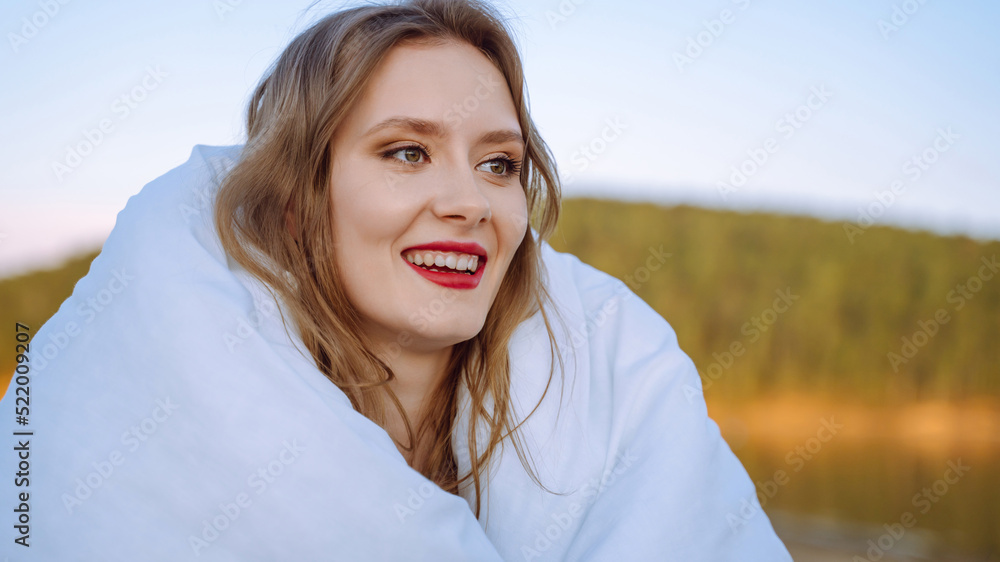 Happy cheerful young woman wearing her red hair wrapped in a blanket standing on the shore rejoicing at positive news Happy cheerful young woman wearing her red hair wrapped in a blanket standing on the shore rejoicing at positive news