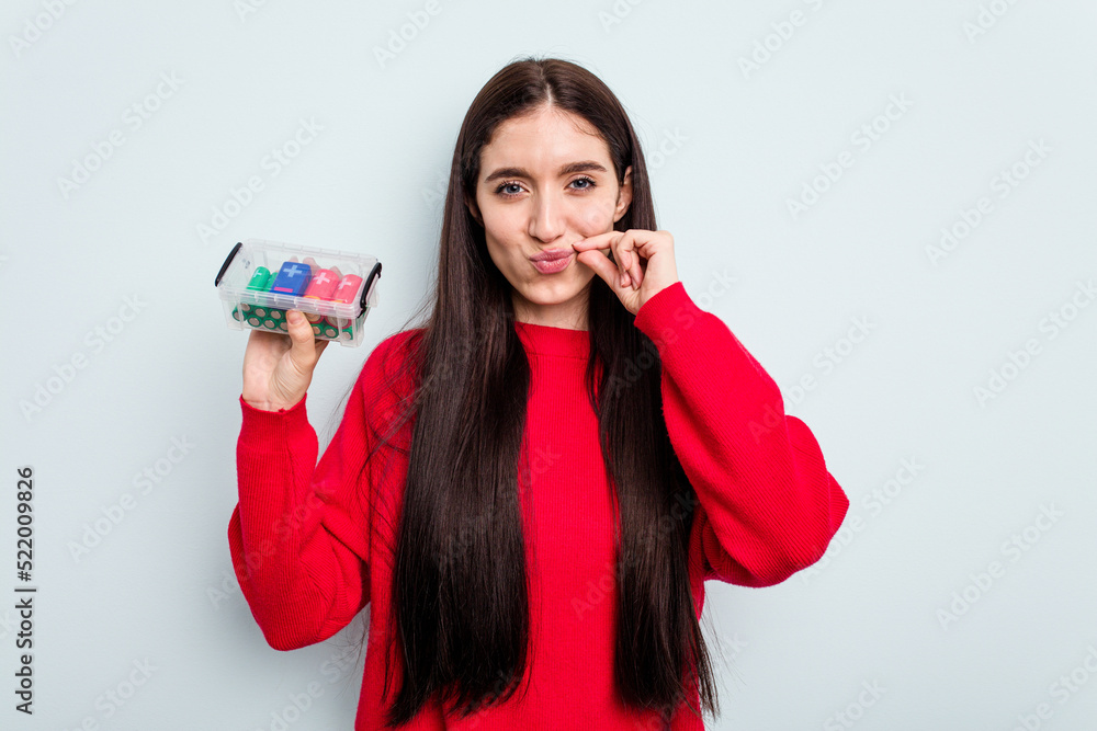 Young caucasian woman holding a batteries box isolated on blue background with fingers on lips keeping a secret.