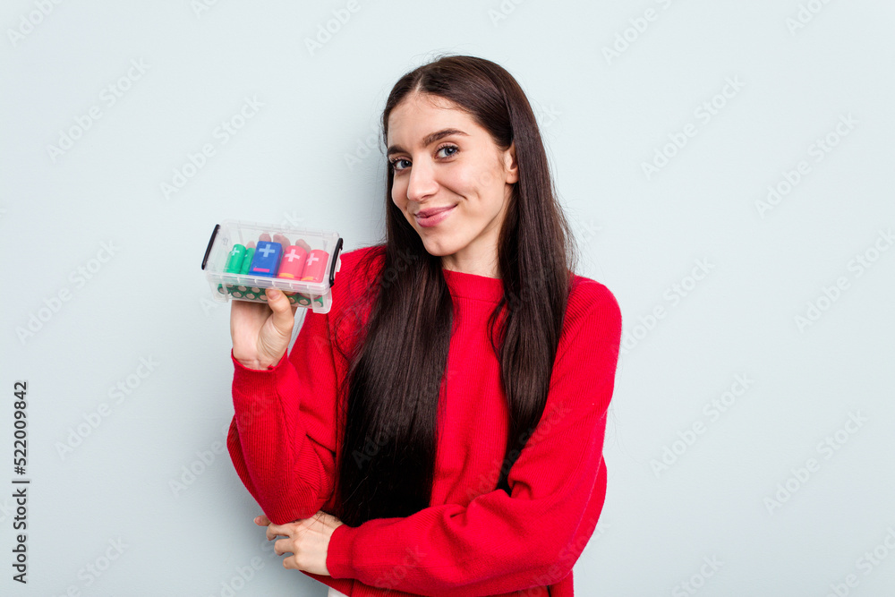 Young caucasian woman holding a batteries box isolated on blue background laughing and having fun. Young caucasian woman holding a batteries box isolated on blue background laughing and having fun.
