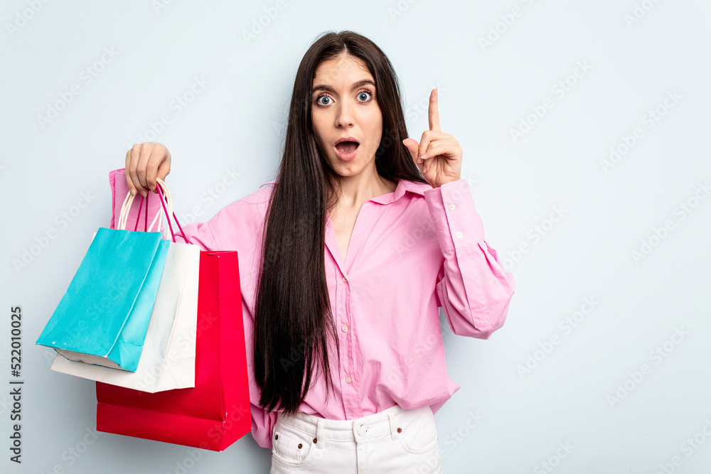 Young caucasian woman going to buy some clothes isolated on blue background having an idea, inspiration concept. Young caucasian woman going to buy some clothes isolated on blue background having an idea, inspiration concept.