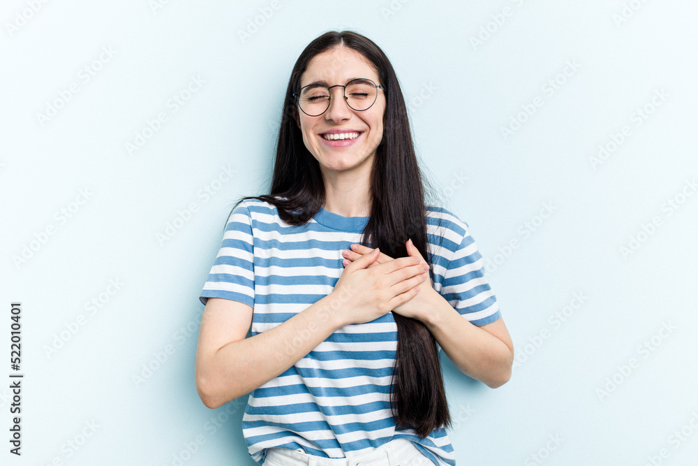 Young caucasian woman isolated on blue background laughing keeping hands on heart, concept of happiness. Young caucasian woman isolated on blue background laughing keeping hands on heart, concept of happiness.