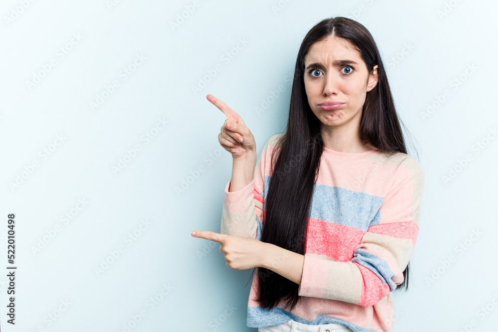Young caucasian woman isolated on blue background shocked pointing with index fingers to a copy space. Young caucasian woman isolated on blue background shocked pointing with index fingers to a copy space.