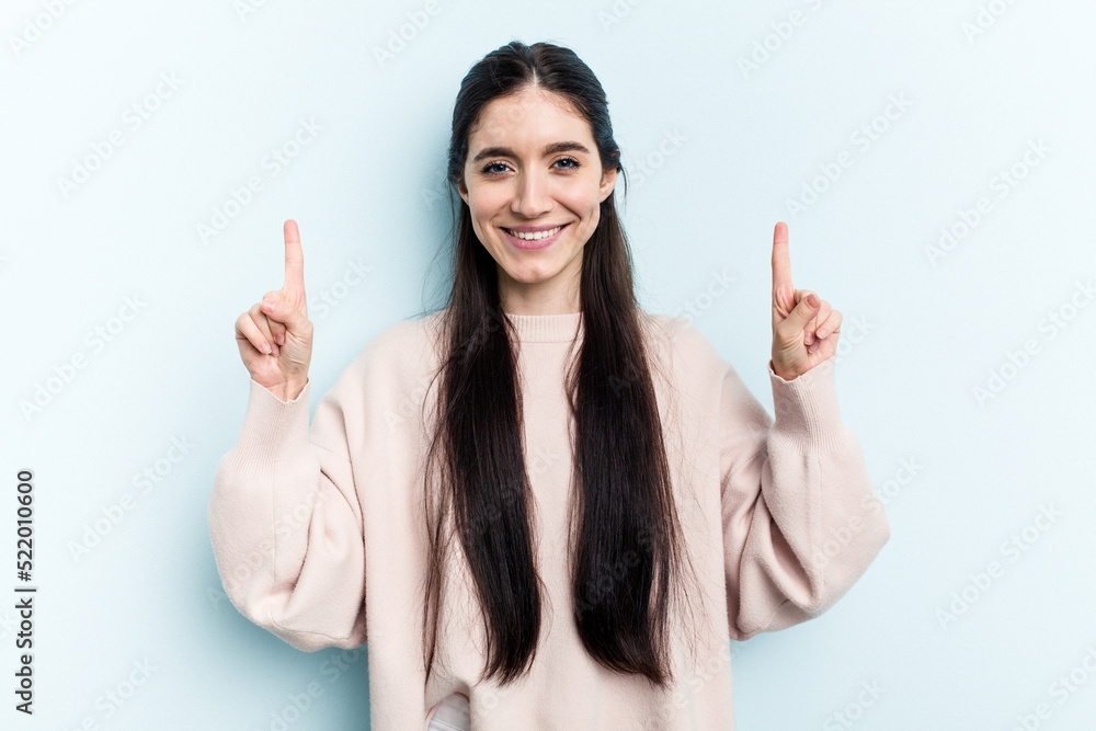 Young caucasian woman isolated on blue background indicates with both fore fingers up showing a blank space. Young caucasian woman isolated on blue background indicates with both fore fingers up showing a blank space.