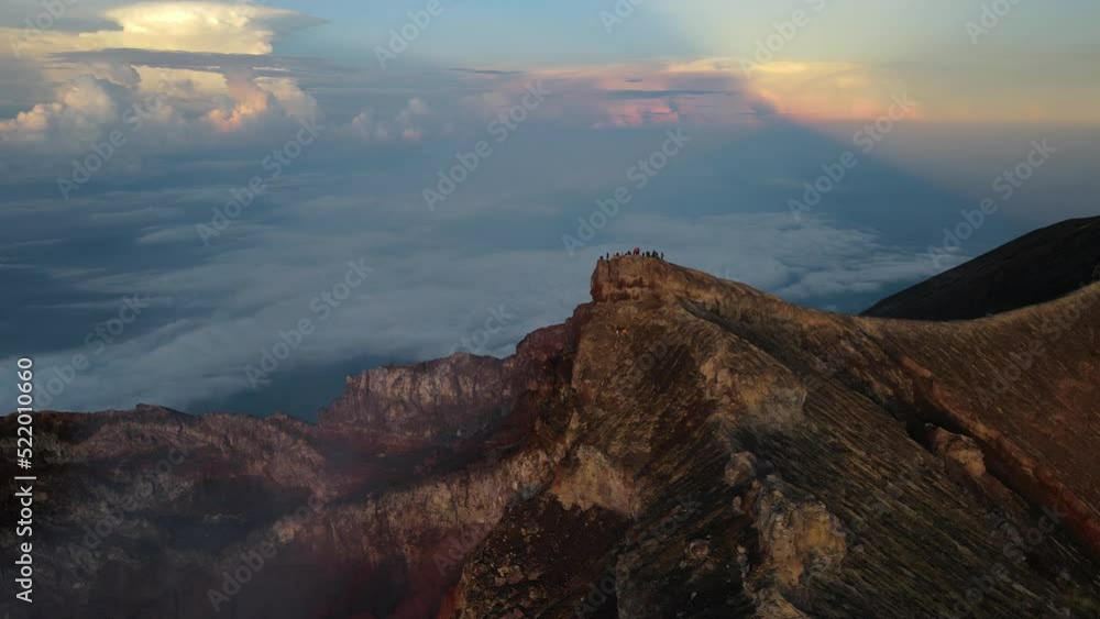 Aerial view of around group of tourists standing on the edge of crater rim of active volcano Mount Agung at sunset. Bali Indonesia Aerial view of around group of tourists standing on the edge of crater rim of active volcano Mount Agung at sunset. Bali Indonesia