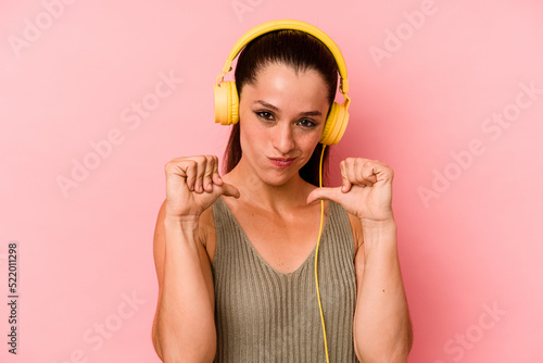 Young caucasian woman listening to music isolated on pink background feels proud and self confident, example to follow.