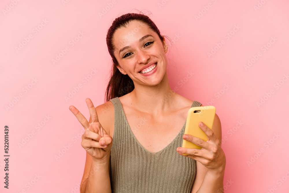 Young caucasian woman holding mobile phone isolated on pink background showing number two with fingers. Young caucasian woman holding mobile phone isolated on pink background showing number two with fingers.