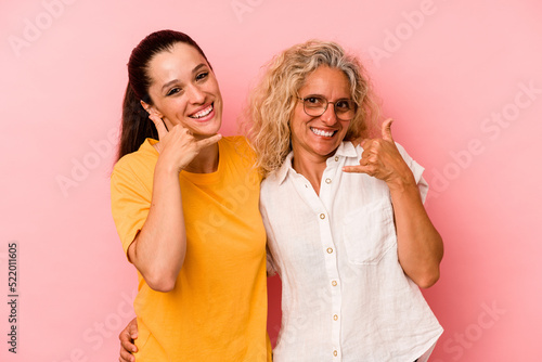 Caucasian mom and daughter isolated on pink background showing a mobile phone call gesture with fingers.