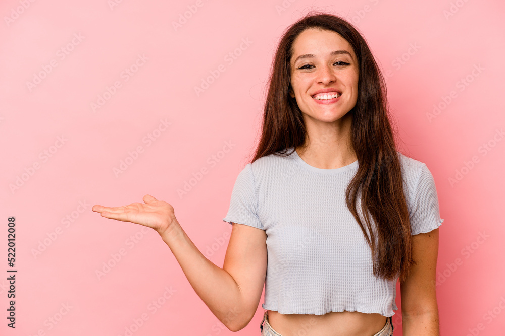 Young caucasian woman isolated on pink background showing a copy space on a palm and holding another hand on waist. Young caucasian woman isolated on pink background showing a copy space on a palm and holding another hand on waist.