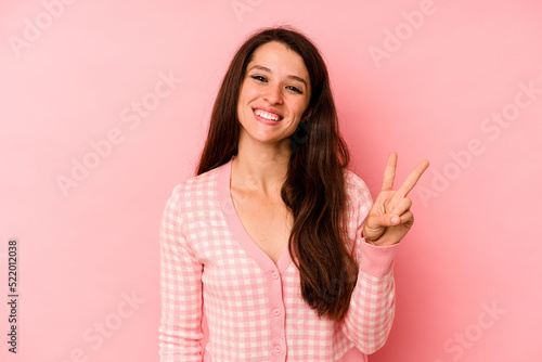 Young caucasian woman isolated on pink background joyful and carefree showing a peace symbol with fingers.