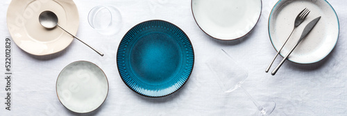 Modern tableware panorama with a vibrant blue plate, cutlery, and glasses, overhead flat lay shot. Trendy dinnerware on tablecloth