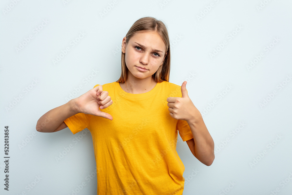 Young caucasian girl isolated on blue background showing thumbs up and thumbs down, difficult choose concept Young caucasian girl isolated on blue background showing thumbs up and thumbs down, difficult choose concept