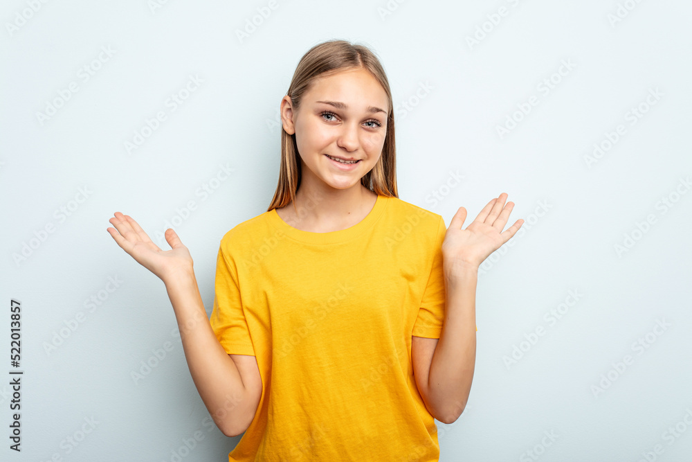 Young caucasian girl isolated on blue background makes scale with arms, feels happy and confident. Young caucasian girl isolated on blue background makes scale with arms, feels happy and confident.