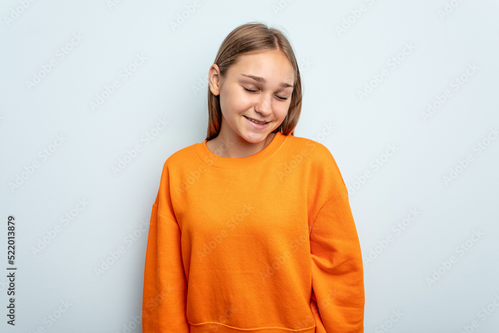 Young caucasian girl isolated on blue background laughs and closes eyes, feels relaxed and happy. Young caucasian girl isolated on blue background laughs and closes eyes, feels relaxed and happy.