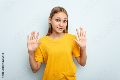 Young caucasian girl isolated on blue background showing number ten with hands. © Asier