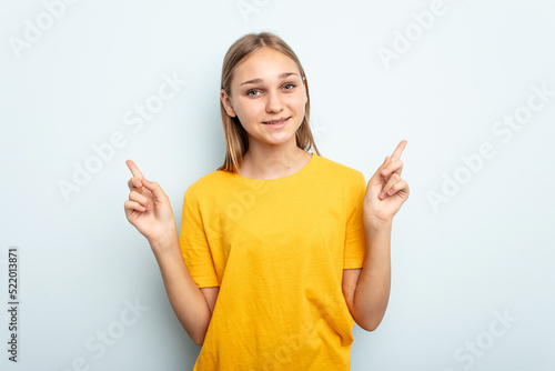 Young caucasian girl isolated on blue background pointing to different copy spaces, choosing one of them, showing with finger. © Asier