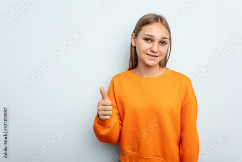 Young caucasian girl isolated on blue background smiling and raising thumb up