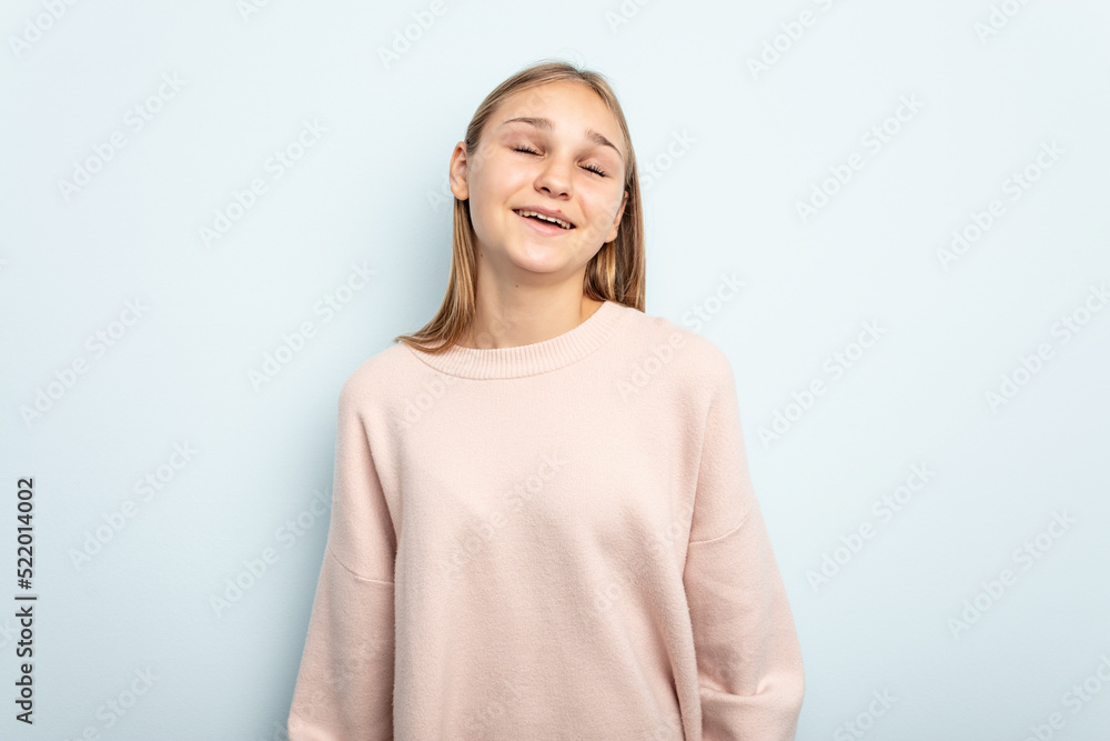 Young caucasian girl isolated on blue background relaxed and happy laughing, neck stretched showing teeth. Young caucasian girl isolated on blue background relaxed and happy laughing, neck stretched showing teeth.