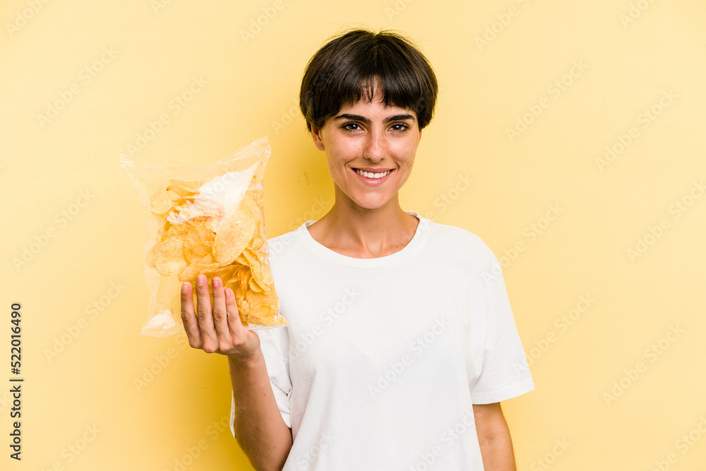 Young caucasian man holding crisps isolated on yellow background happy, smiling and cheerful. Young caucasian man holding crisps isolated on yellow background happy, smiling and cheerful.