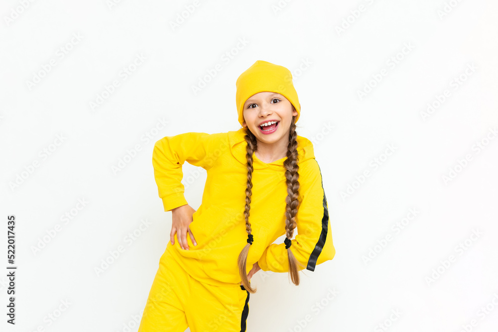 A child in a tracksuit and a yellow hat. A beautiful little teenage girl with braids and a wide smile on a white isolated background. A child in a tracksuit and a yellow hat. A beautiful little teenage girl with braids and a wide smile on a white isolated background.