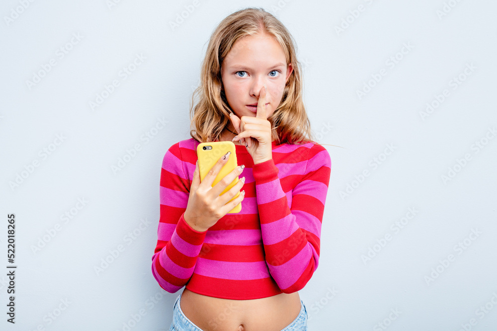 Caucasian teen girl holding mobile phone isolated on blue background keeping a secret or asking for silence. Caucasian teen girl holding mobile phone isolated on blue background keeping a secret or asking for silence.