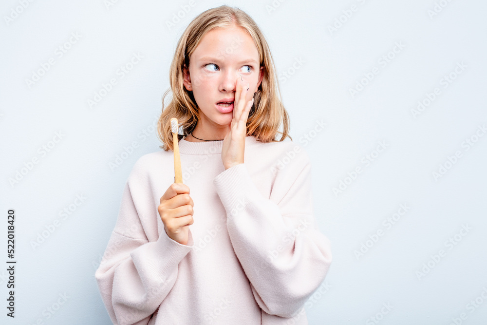 Caucasian teen girl holding a toothbrush isolated on blue background is saying a secret hot braking news and looking aside Caucasian teen girl holding a toothbrush isolated on blue background is saying a secret hot braking news and looking aside