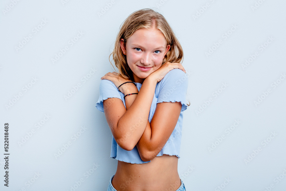 Naklejka premium Caucasian teen girl isolated on blue background hugs, smiling carefree and happy.