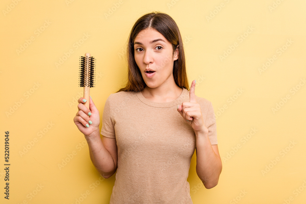 Young caucasian woman holding a brush hair isolated on yellow background having an idea, inspiration concept. Young caucasian woman holding a brush hair isolated on yellow background having an idea, inspiration concept.