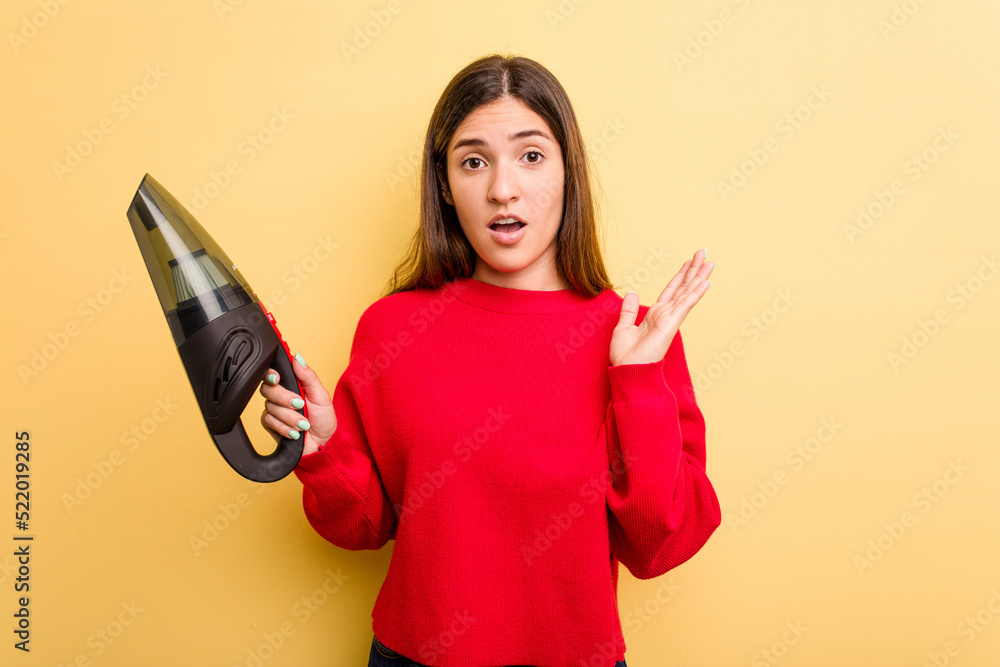 Naklejka premium Young caucasian woman holding a hand vacuum cleaner isolated on yellow background surprised and shocked.
