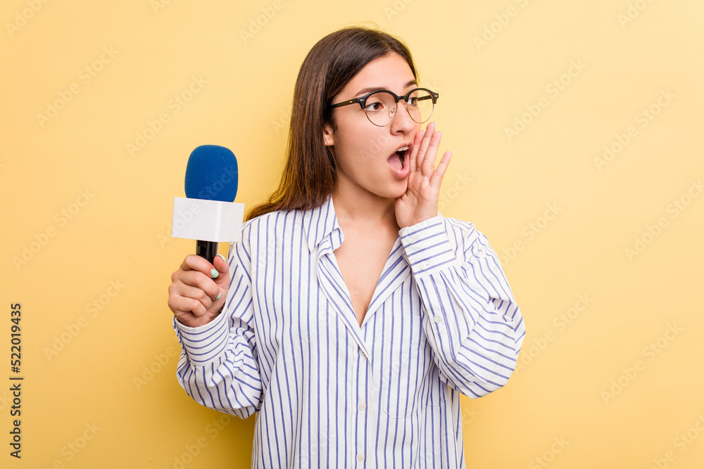 Young caucasian presenter TV woman isolated on yellow background shouting and holding palm near opened mouth. Young caucasian presenter TV woman isolated on yellow background shouting and holding palm near opened mouth.