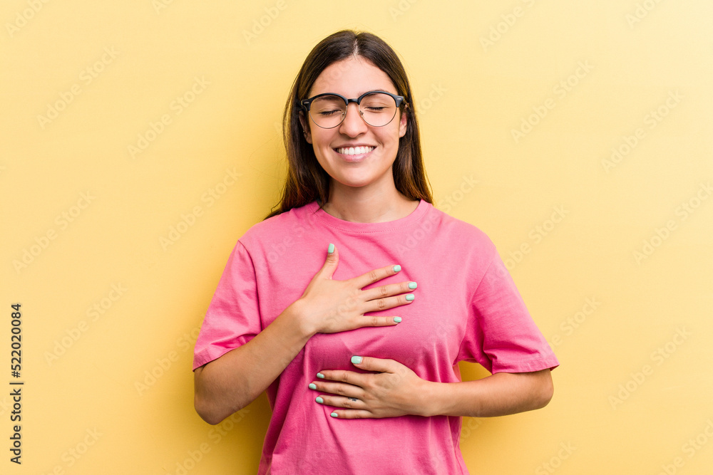 Obraz premium Young caucasian woman isolated on yellow background laughs happily and has fun keeping hands on stomach.