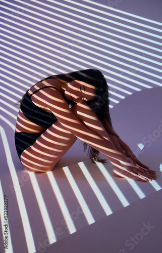 Sitting on the floor. Beautiful young woman is in projector neon lights in the studio